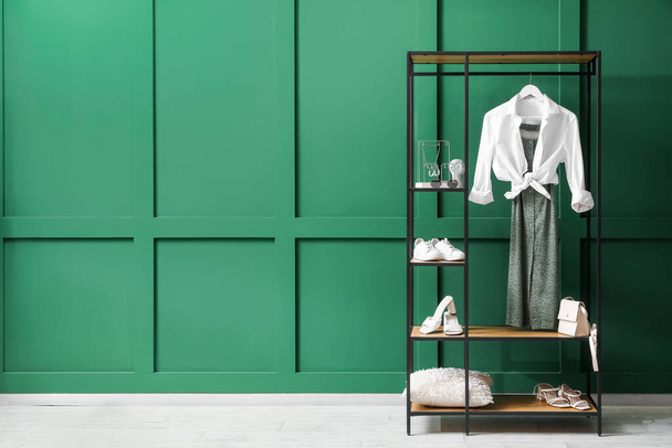Odadaki yeşil duvarın yanında giysi, ayakkabı ve aksesuarlı raf ünitesi. - Fotoğraf, Görsel