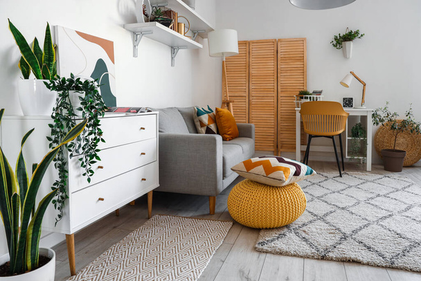 Интерьер стильной гостиной с уютным диваном, комодом и удобным рабочим местом - Фото, изображение