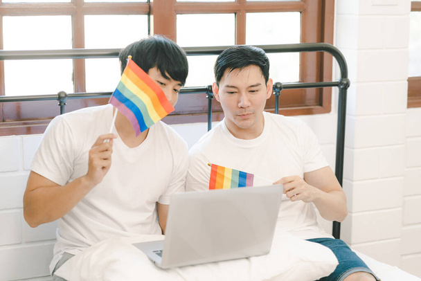 幸せな婚約したアジアのゲイのカップルは、 LGBTの虹の旗を振って、 VDOは寝室で幸せな瞬間を共有するために呼び出します。幸せな結婚した同性愛者のカップル。若いですアジアゲイカップル感じ幸せなショーリングにホーム. - 写真・画像