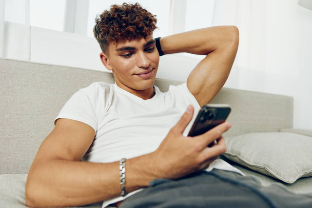 Mann Interieur Internet Home Sitzen hält moderne Selfies Nachricht Telefon Smartphone Couch Technologie Text glückselig Cyberspace mit Attrappe Lächeln SMS - Foto, Bild