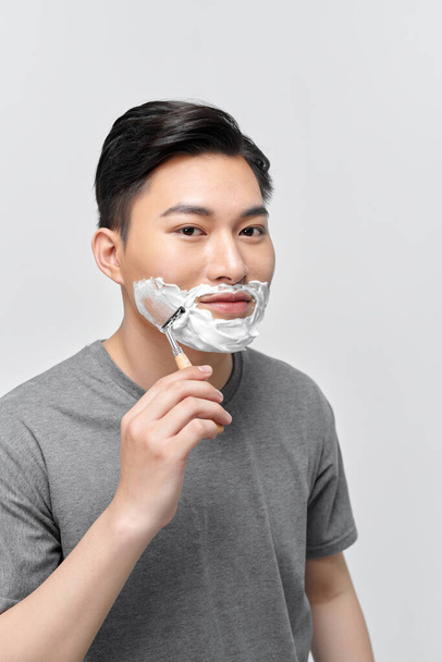 handsome man using shaving foam before shaving while standing in front of bathroom mirror - Zdjęcie, obraz