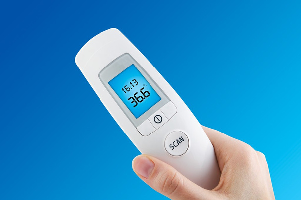 Hand holding digital contactless thermometer on blue background - Photo, Image