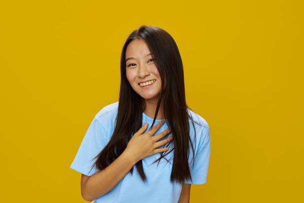 Азіатська жінка посміхається зубами руками жести, знаки і символи на жовтому тлі в синій футболці і джинсах. Високоякісна фотографія - Фото, зображення