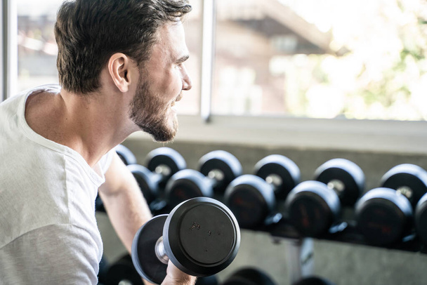 Slimme sportman tilt halter in fitnessstudio gezonde levensstijl - Foto, afbeelding