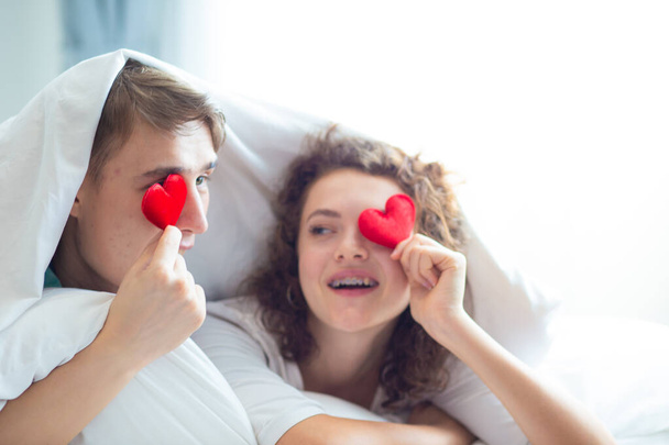Ερωτικό ζευγάρι ξαπλωμένο σε λευκό κρεβάτι κουβέρτα κρατήστε το σύμβολο της καρδιάς Valentine έννοια - Φωτογραφία, εικόνα