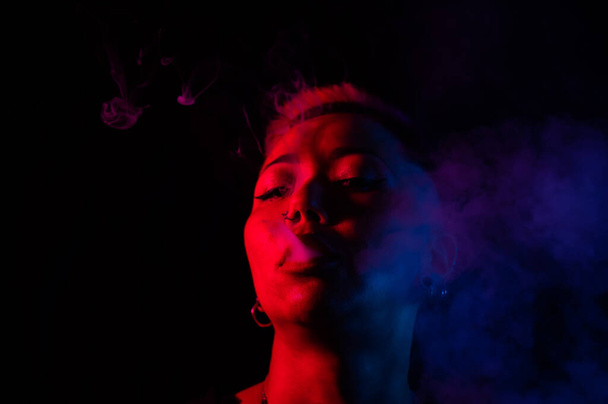 Close up portrait of asian woman with short hair smoking in neon light - Fotó, kép