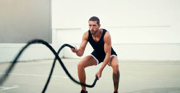 Man, fitness and battle rope exercise for physical training, workout or wellness in the outdoors. Fit, active and serious male person exercising with ropes for intense endurance, stamina or cardio. - Photo, Image