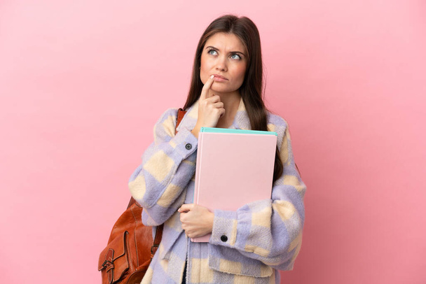 Junge Studentin isoliert auf rosa Hintergrund mit Zweifeln beim Nachschauen - Foto, Bild