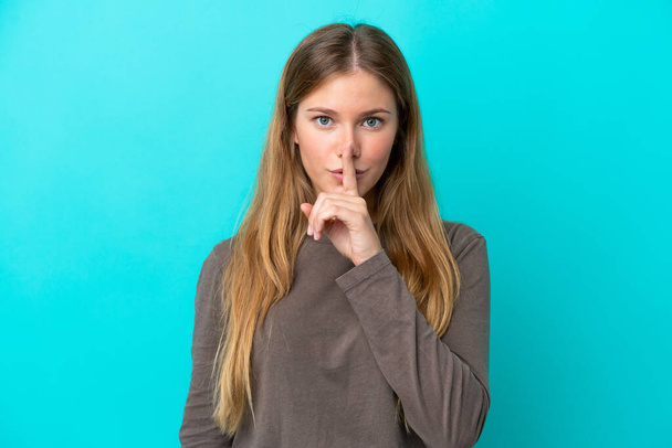 Young blonde woman isolated on blue background showing a sign of silence gesture putting finger in mouth - Foto, afbeelding
