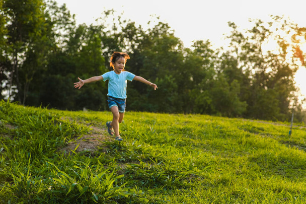 Šťastná holčička běhá po trávě v letním parku. Holčička běží loukou se západem slunce. - Fotografie, Obrázek