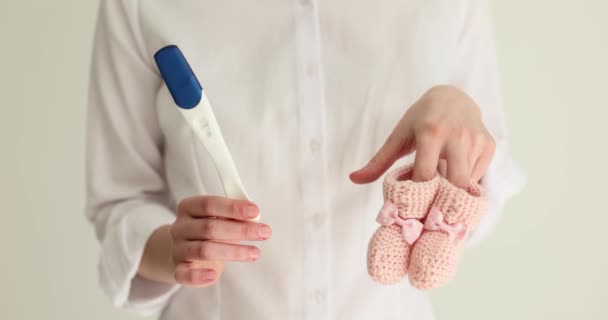 En las manos de las mujeres prueba de embarazo y los niños pequeños zapatillas de color rosa. Planificación del embarazo - Imágenes, Vídeo