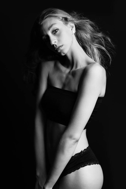 Sexy blonde woman portrait with black underwear isolated on dark background. Studio portrait. Black and white. - Фото, изображение