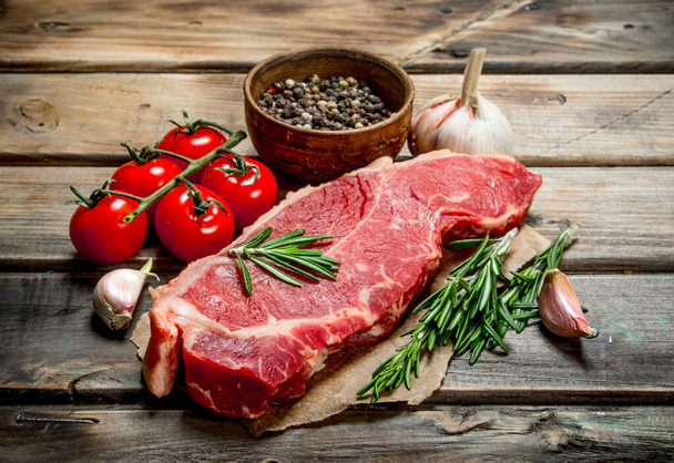 Raw steak with rosemary, tomatoes and aromatic spices. On a wooden background. - Foto, Imagem