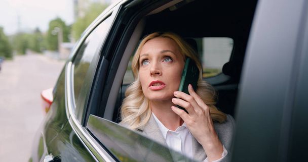 Beautiful blond woman tourist traveling in a taxi or personal car and talking on smartphone, view through the car window. - 写真・画像