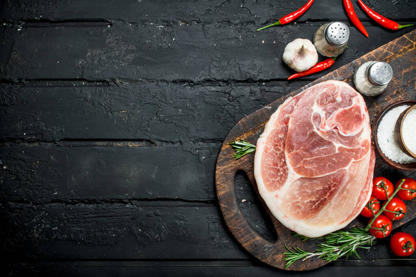 Big raw pork steak with spices and vegetables. On a black rustic background. - Foto, immagini