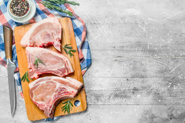 Raw pork steak on the bone with rosemary on the napkin. On a rustic background. - Fotoğraf, Görsel