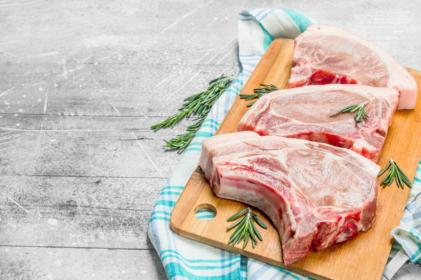 Raw pork steak on the bone with rosemary on the napkin. On a rustic background. - Photo, Image