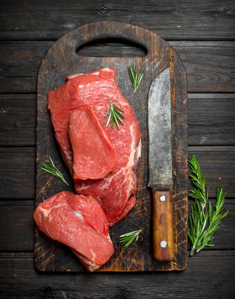 Raw meat. Sliced beef with rosemary and old hatchet. On a wooden background. - Foto, afbeelding