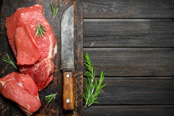 Raw meat. Sliced beef with rosemary and old hatchet. On a wooden background. - Фото, изображение
