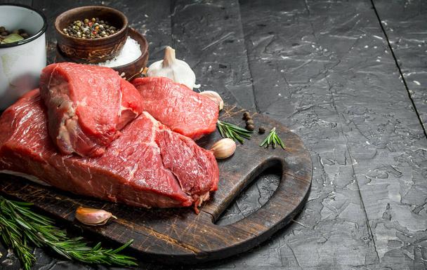 Raw meat. Pieces of beef with spices and herbs on a wooden Board. On a black rustic background. - Fotografie, Obrázek