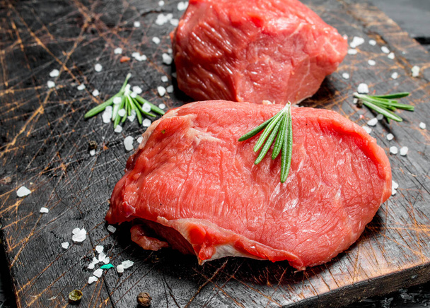 Raw meat. Pieces of fresh beef with salt and rosemary. On a wooden background. - Photo, Image