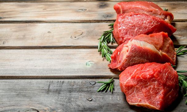 Raw meat. Pieces of beef with rosemary branches. On a wooden background. - Foto, afbeelding