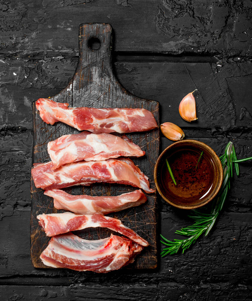 Raw sliced ribs with tomato sauce and spices . On a black rustic background. - Fotó, kép