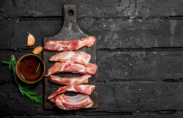 Raw sliced ribs with tomato sauce and spices . On a black rustic background. - Fotó, kép