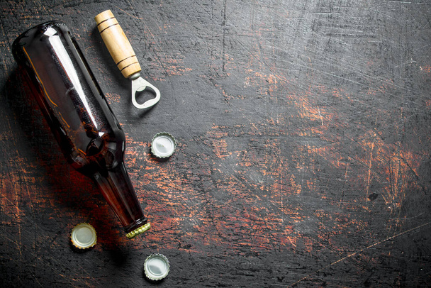 Glass beer bottle and opener. On dark rustic background - Fotó, kép
