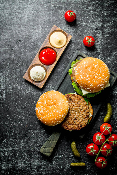 Burgers with French fries, gherkins,tomatoes and different sauces. On rustic background - Foto, immagini