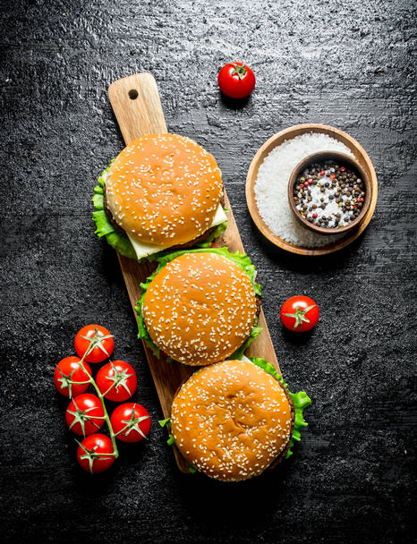 Burgers on a wooden stand with spices and tomatoes. On black rustic background - Photo, image