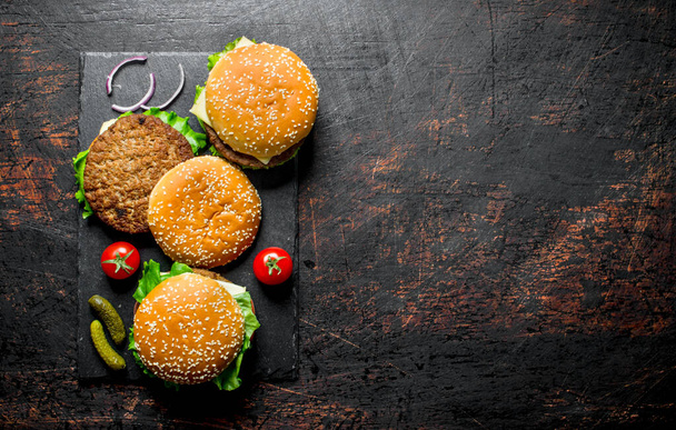 Burger mit Rindfleisch, Tomaten und Gurken auf schwarzem rustikalem Hintergrund - Foto, Bild
