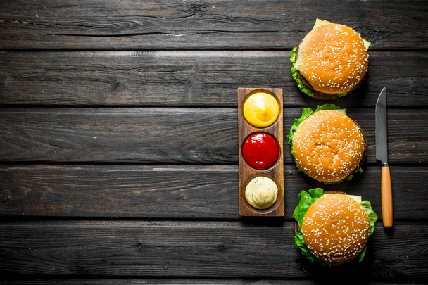 Burgers with different sauces and a knife. On black wooden background - Foto, imagen