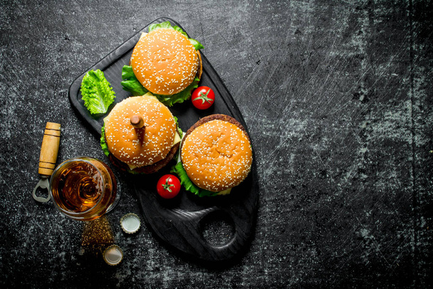 Burgers with a knife and beer in a glass. On black rustic background - Foto, Imagem