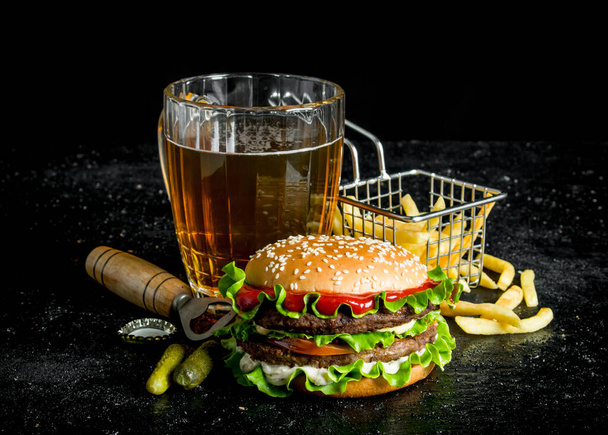 Burger with beer, fries and gherkins. On black rustic background - Photo, image