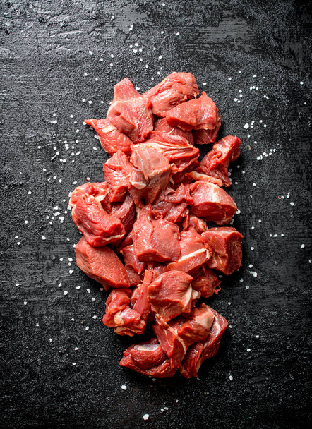 Sliced raw beef with salt grains. On black rustic background - Valokuva, kuva
