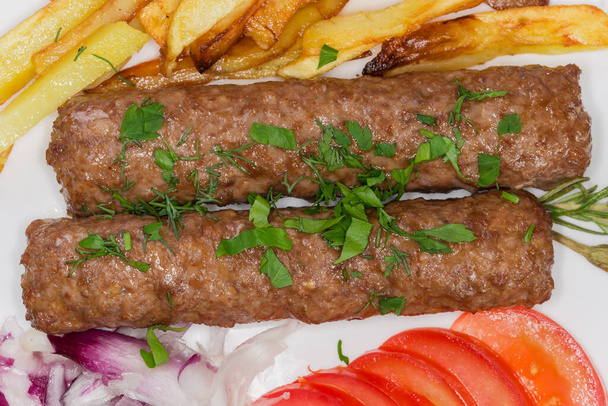 Twee gebakken lula kebab met frietjes en gehakte groenten op de schotel, bovenaanzicht close-up - Foto, afbeelding