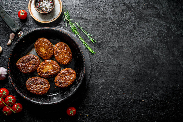 Cutlets in pan with rosemary, garlic and tomatoes. On black rustic background - Foto, immagini