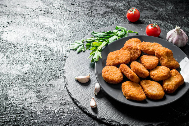 Chicken nuggets with parsley and garlic cloves. On black rustic background - Foto, Imagen