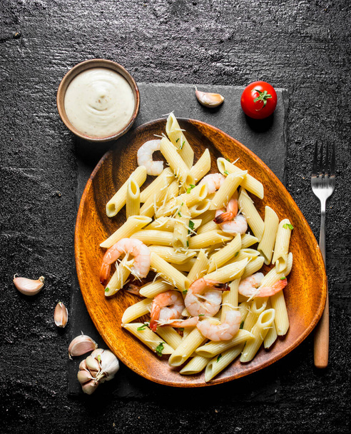 Pasta with shrimp in a wooden plate and the sauce in a bowl. On black rustic background - Fotografie, Obrázek
