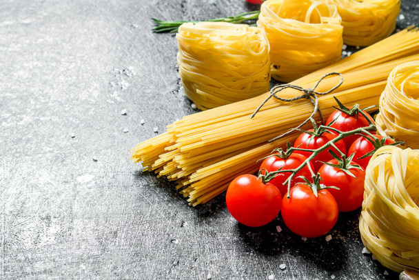 Spaghetti and tagliatelle raw with tomatoes. On black rustic background - Foto, Imagen