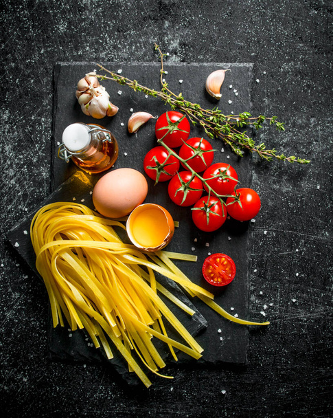 Home made raw pasta with thyme, eggs, oil and tomatoes. On black rustic background - Foto, afbeelding