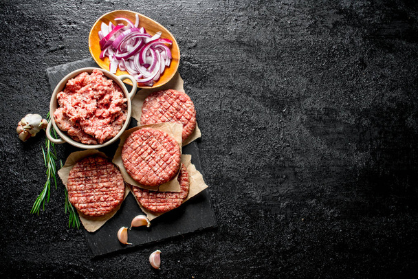 Raw burgers with ground beef and sliced onions in bowls. On black rustic background - Foto, Bild