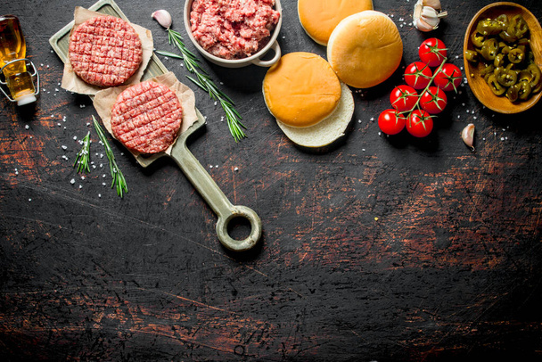 生のハンバーガーと牛肉、パン、トマト。暗い素朴な背景に - 写真・画像