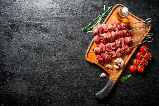 Raw kebab on a cutting Board with tomatoes, garlic ,rosemary and oil. On black rustic background - 写真・画像