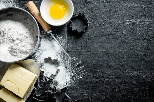 Baking background. Flour with egg, butter and various forms for baking. On black rustic background - Foto, Imagen