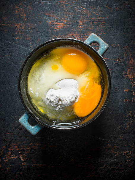 Flour with eggs in the pan. On dark rustic background - Foto, Bild