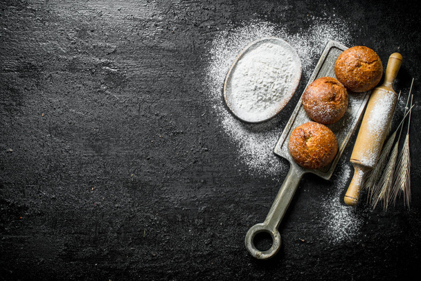 Fragrant buns with flour and rolling pin. On black rustic background - Фото, зображення