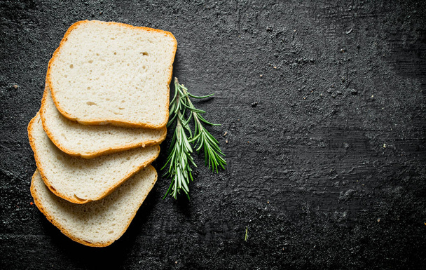 Pieces of fresh bread with rosemary. On black rustic background - Fotoğraf, Görsel