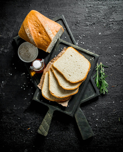 Bread with rosemary and oil on the cutting Board. On black rustic background - 写真・画像